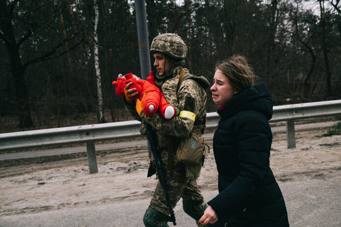 Foto eines Soldaten mit einem Baby auf dem Arm und Frau die nebenher läuft